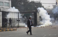 An angry lawyer runs for shelter after police fire tear gas shell to disperse them during a clash in Lahore, Pakistan, Wednesday, Dec. 11, 2019. Hundreds of Pakistani lawyers, angered over alleged misbehavior of some doctors toward one of their colleagues last month, stormed a cardiology hospital in the eastern city of Lahore, setting off scuffles with the facility's staff and guards that left heart patients unattended for several hours. (AP Photo/K.M. Chaudary)