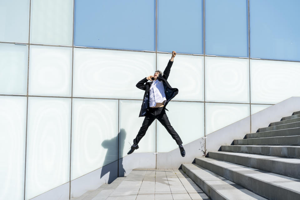 Excited businessman on cell phone jumping in the city