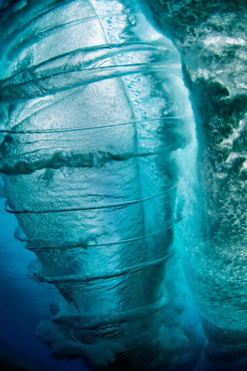 In this image called "Hornado," while swimming under a big wave, Clark points his camera upwards to photograph the mysterious phenomenon of rib vortices, the thin twisters spinning around tubes and which can only be seen from below the surface.