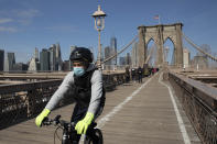 A cyclist wears a mask as he crosses the Brooklyn Bridge, Monday, March 16, 2020 in New York. The bridge's pedestrian and bicycle path is normally crowded on a sunny day. (AP Photo/Mark Lennihan)