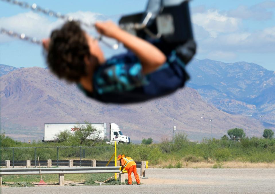 A prisoner trims weeds around a parking lot as a child plays on a swing at Keiller Park in Willcox on June 22, 2022.