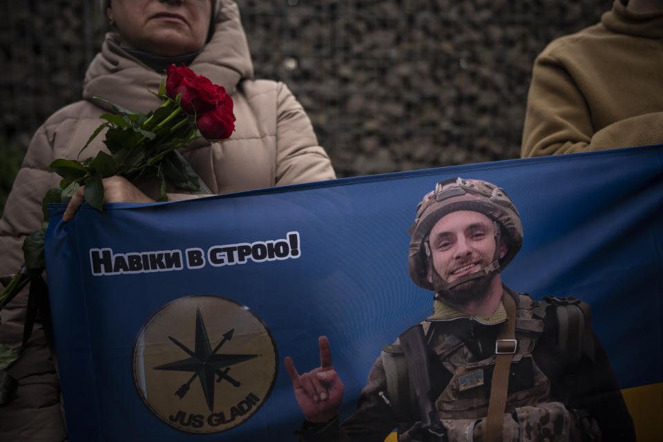 People hold a flag with a picture of Ukrainian soldier Oleksandr Hrianyk at his funeral in Kyiv, Ukraine, Saturday, Oct. 28, 2023. Hrianyk died in battle in May 2022 in the city of Mariupol, but was only cremated recently after his remains were found and identified. (AP Photo/Bram Janssen)