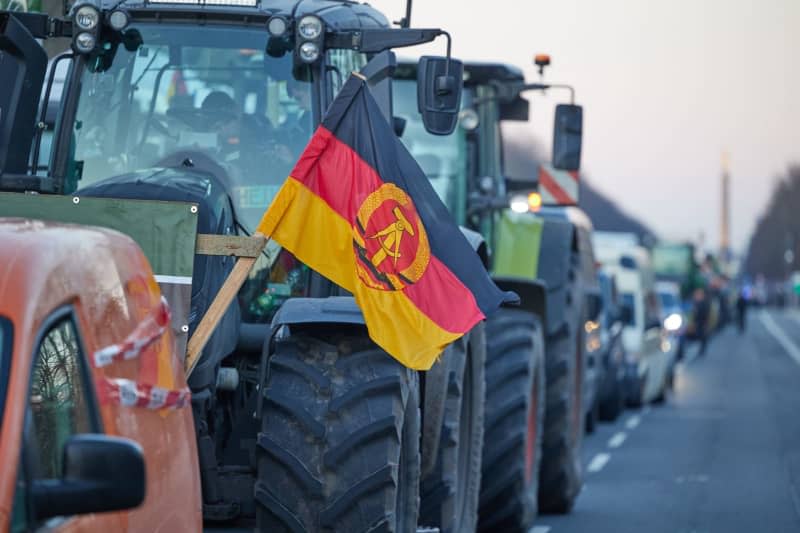 A GDR flag can be seen during a farmers' protest in front of the Brandenburg Gate. In response to the federal government's austerity plans, the farmers' association has called for a week of action with rallies and rallies starting on January 8. It is to culminate in a major demonstration in the capital on January 15. Jörg Carstensen/dpa