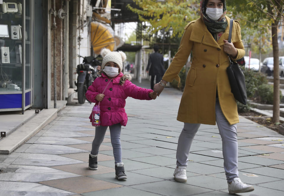 A girl and a woman wearing protective face masks to help prevent the spread of the coronavirus walk on a sidewalk in downtown Tehran, Iran, Saturday, Dec. 5, 2020. Iran's death toll from the global pandemic has risen above 50,000, according to state television, as the country grapples with the worst outbreak in the Middle East. (AP Photo/Vahid Salemi)