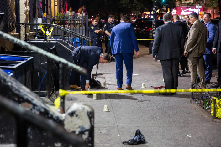 A dozen police officers wearing uniforms or suits stand on a sidewalk roped off with yellow tape.