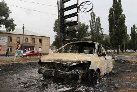 A woman walks past a car burned during fighting between pro-Russian separatists and Ukrainian forces in the eastern Ukrainian town of Torez August 28, 2014. REUTERS/Maxim Shemetov