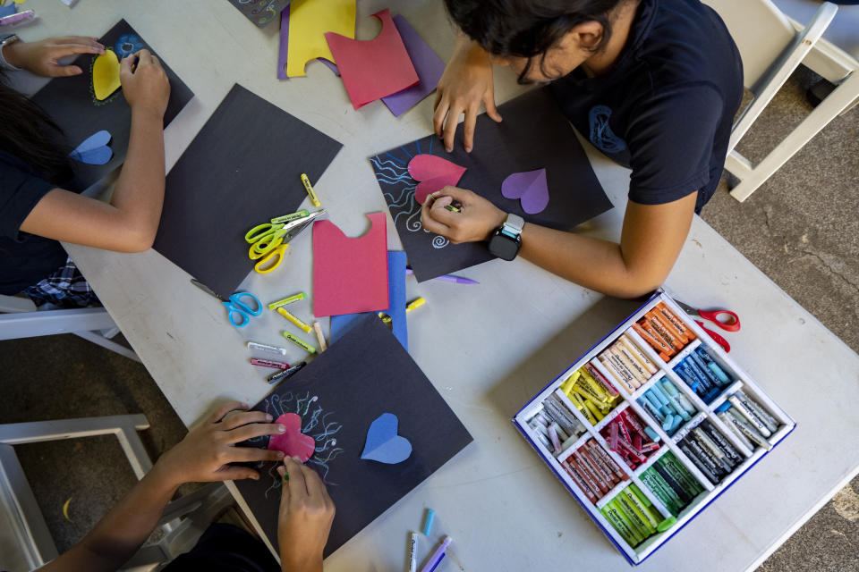 Sacred Hearts School fifth grade students draw around hearts at their temporary school site at Sacred Hearts Mission Church on Tuesday, Oct. 3, 2023, in Lahaina, Hawaii. Sacred Hearts and other private schools across the state took in displaced public school students. The three public schools that survived the deadly August wildfire are set to reopen this week (AP Photo/Mengshin Lin)