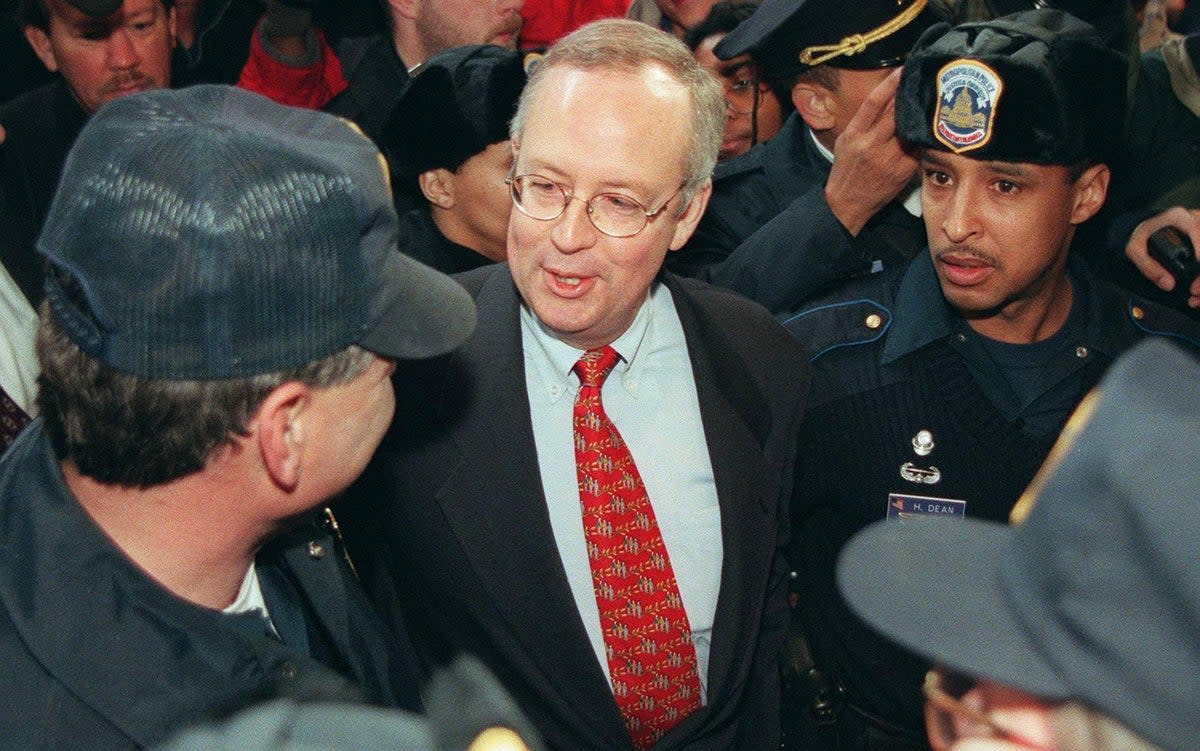 Kenneth Starr, independent counsel, speaks to a Washington, DC police officer as he is escorted away after speaking at a press conference on 22 January 1998 (LUKE FRAZZA/AFP via Getty Images)