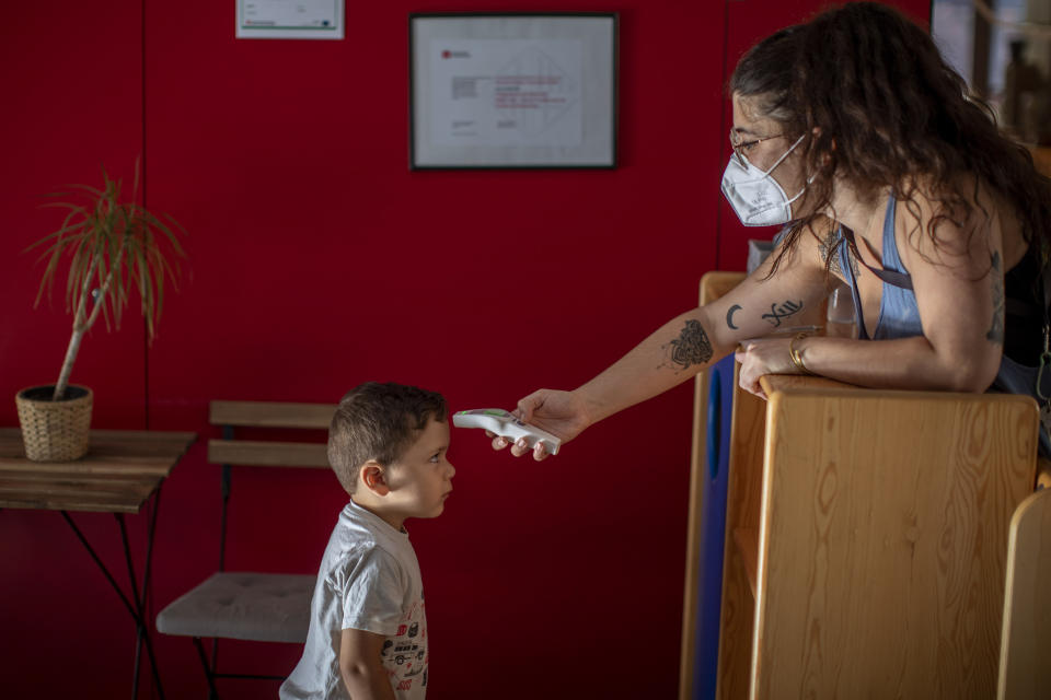 Hugo, de 3 años, se mantiene quieto mientras una maestra le toma la temperatura luego de llegar al jardín de infantes Cobi en Barcelona, España, el viernes 26 de junio de 2020. (AP Foto/Emilio Morenatti)