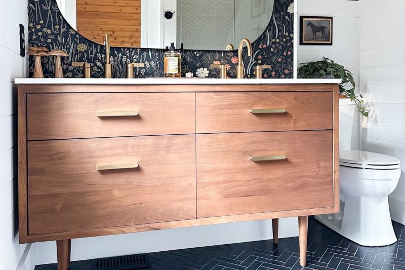 Bathroom with wood drawers, double sinks, and navy botanical wallpaper