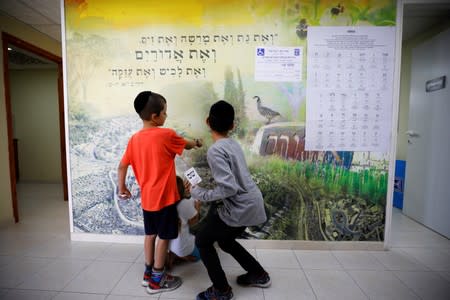 A boy holds a ballot slip as he plays with another boy during Israel's parliamentary election, near a polling station in the Israeli settlement of Adora, in the occupied West Bank