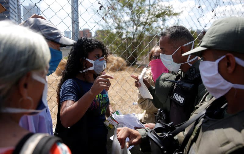 People wearing protective masks in front of a supermarket while the National Guard controls their access in Caracas