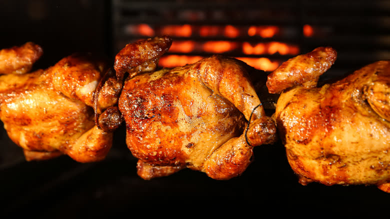 Three rotisserie chickens on spit in oven