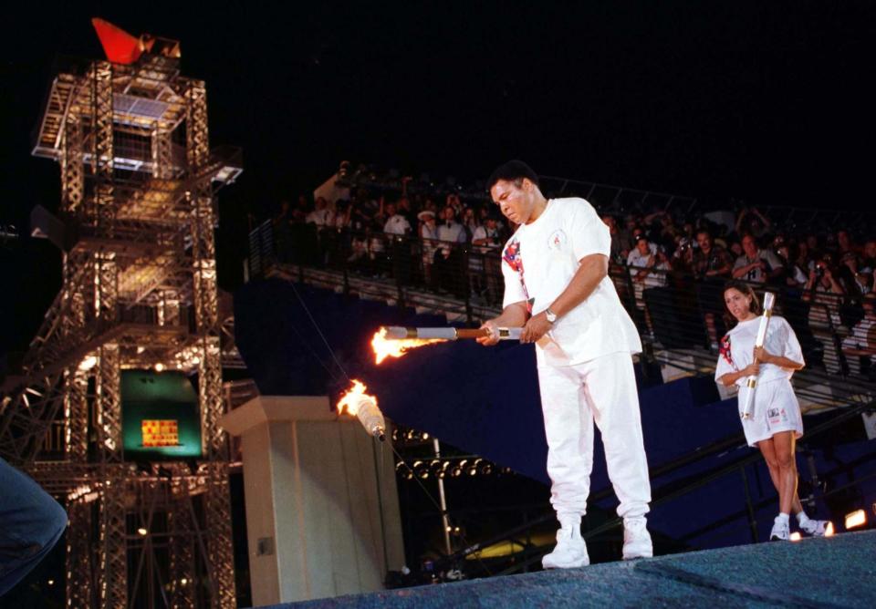 El ex boxeador olímpico Muhammad Ali enciende el dispositivo que luego encenderá el pebetero olímpico para coronar las ceremonias de apertura de los Juegos Olímpicos de Verano de 1996 en Atlanta el 19 de julio. La nadadora estadounidense Janet Evans (derecha) observa después de entregarle la antorcha a Ali. (Reuters)