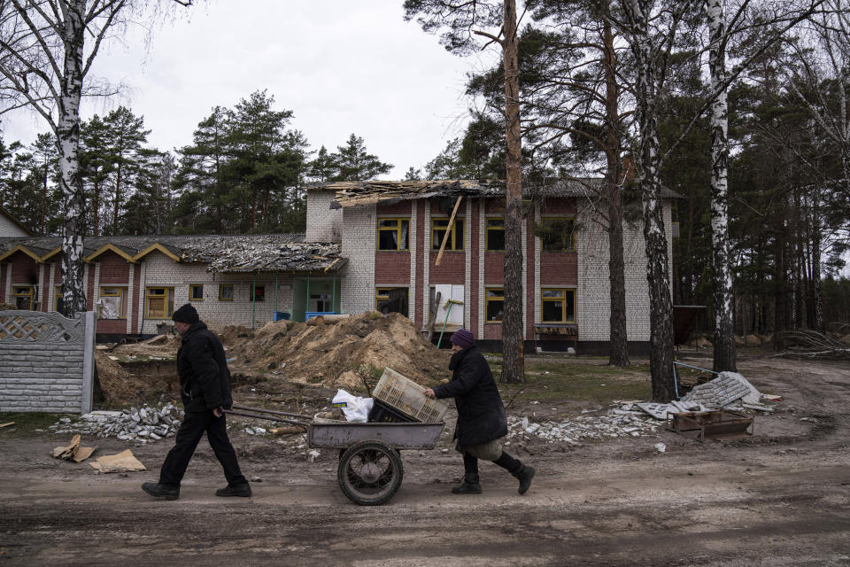 A man and his wife push a cart with food past a school damaged by shelling in Yahidne, near of Dnipro, Ukraine, Tuesday, April 12, 2022. (AP Photo/Evgeniy Maloletka)