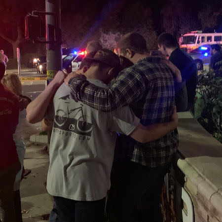 People stand behind cordon tape and hold each other, after the shooting in Thousand Oaks, California, U.S. November 8, 2018 in this image obtained from social media. BULA PRODUCTIONS/via REUTERS
