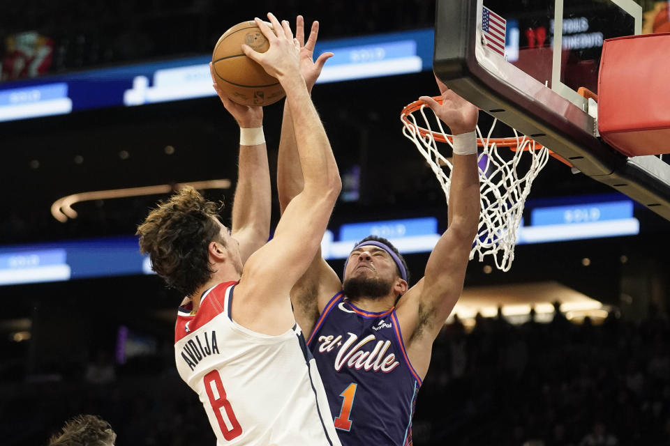 Phoenix Suns' Devin Booker (1) attempts to block a shot by Washington Wizards' Deni Avdija (8) during the second half of an NBA basketball game in Phoenix, Sunday, Dec. 17, 2023. (AP Photo/Darryl Webb)