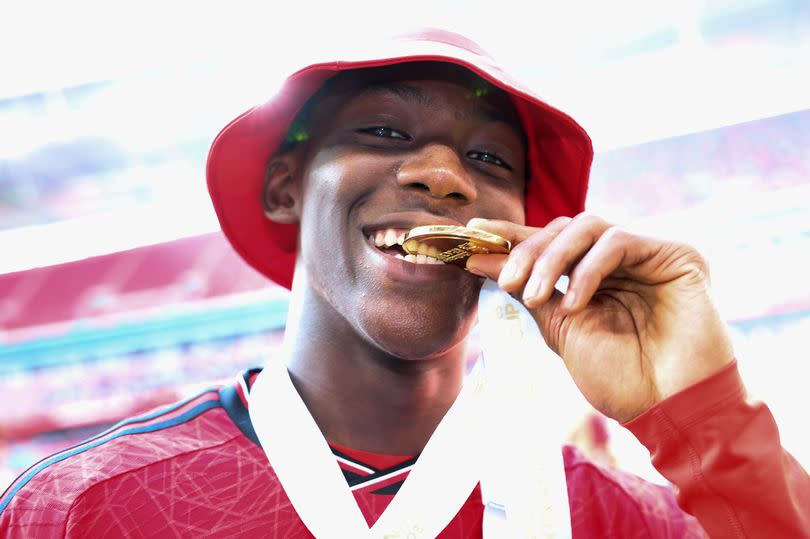 Kobbie Mainoo bites his FA Cup winners medal with a bucket hat on.