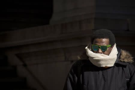 A man stands in a small patch of sunlight on the steps of Federal Hall to warm up on a cold and windy day in New York's financial district February 13, 2015. REUTERS/Brendan McDermid