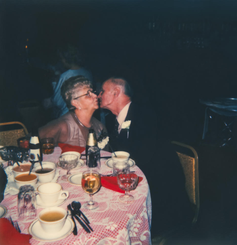 Elderly couple sharing a kiss at a dining table set with cups and dishes