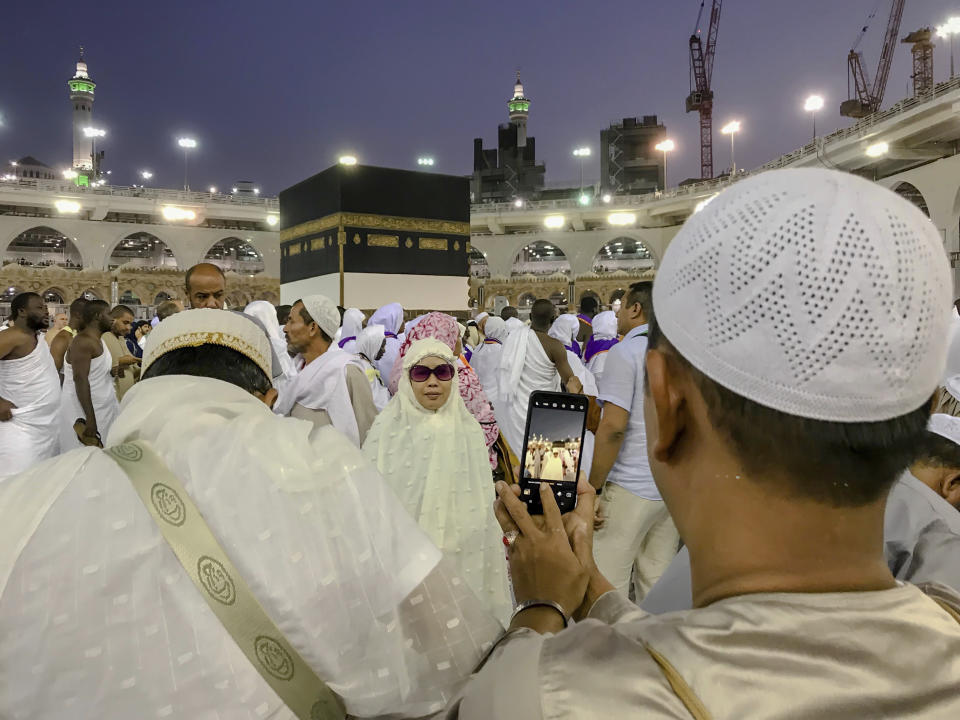 A Muslim pilgrim takes a photograph of his relative near the Kaaba, the cubic building at the Grand Mosque, in the Muslim holy city of Mecca, Saudi Arabia, Friday, Aug. 17, 2018. The annual Islamic pilgrimage draws millions of visitors each year, making it the largest yearly gathering of people in the world. (AP Photo/Dar Yasin)