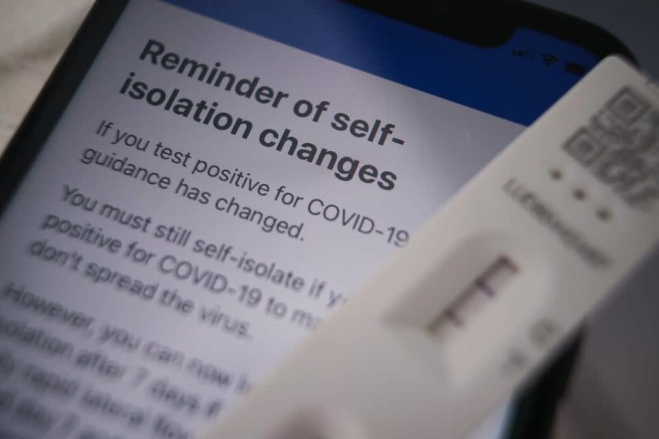 A positive lateral flow test cassette placed next to advice from the NHS Covid app on an iPhone, in London (Yui Mok/PA) (PA Wire)