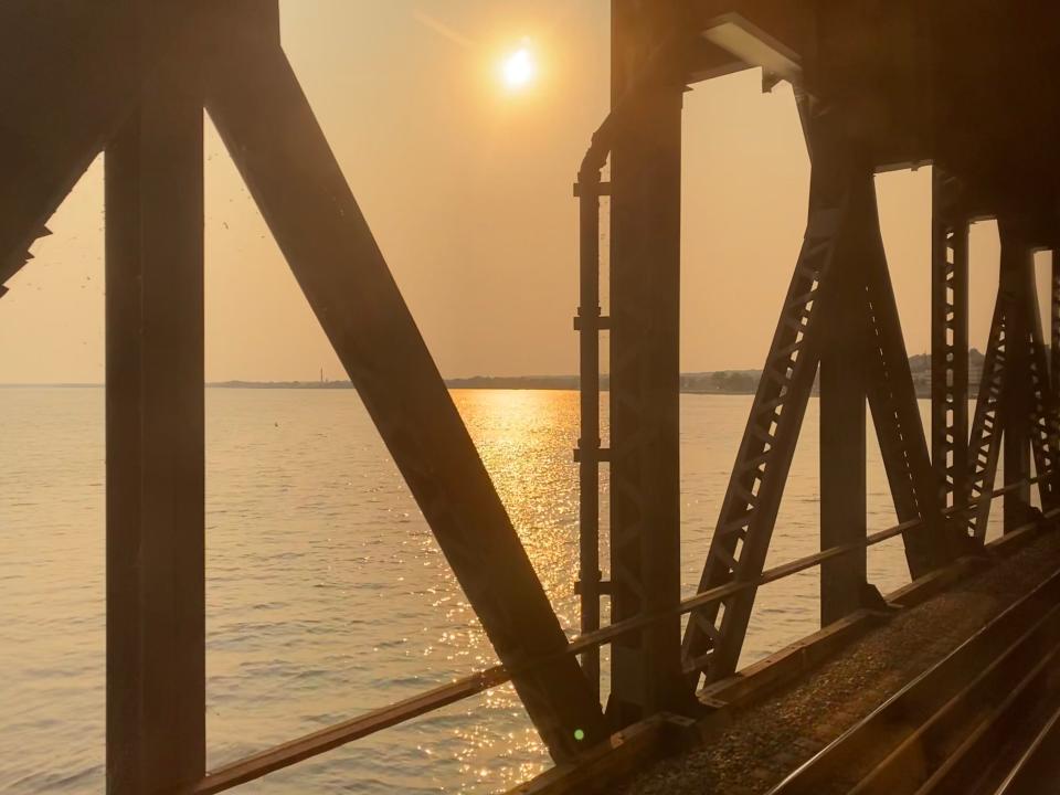 View of sun over water from train tracks on bridge