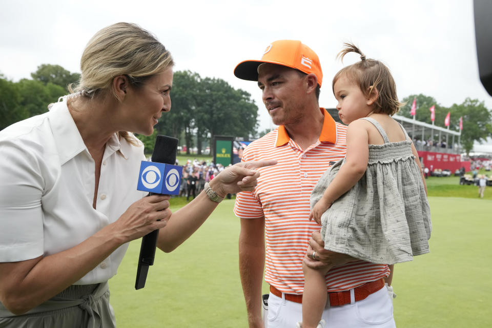 Rickie Fowler holds his daughter, Maya, and is interviewed after winning on the first playoff hole on the 18th green against Collin Morikawa and Adam Hadwin during the final round of the Rocket Mortgage Classic golf tournament at Detroit Country Club, Sunday, July 2, 2023, in Detroit. (AP Photo/Carlos Osorio)