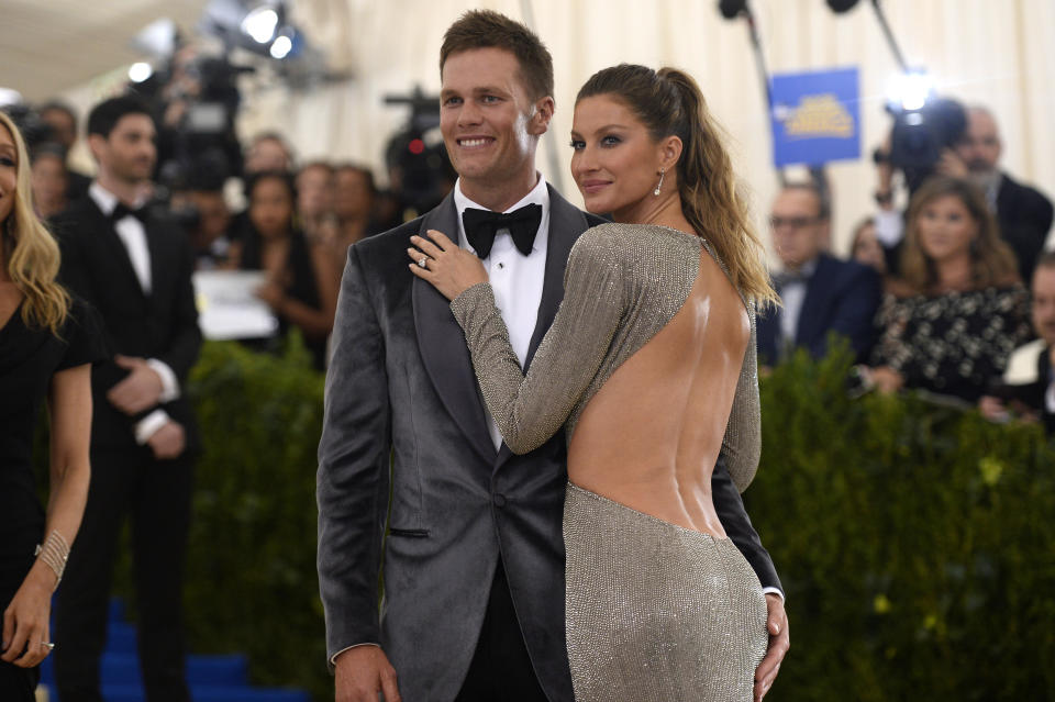 Tom Brady and Gisele Bündchen pose together; he's in a suit and bow tie, she wears a backless dress, at a red carpet event