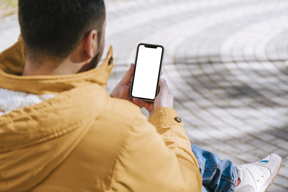 unrecognizable man sitting on a street bench while ordering food for delivery. White screen.