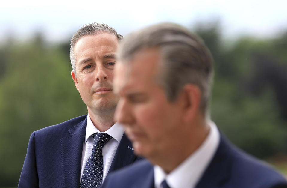 FILE - In this Tuesday, June 8, 2021 file photo, Democratic Unionist Party member Paul Givan, background, looks at party leader Edwin Poots during a press conference at Stormont Buildings parliament in Belfast, Northern Ireland. Northern Ireland’s biggest political parties appear set to agree on a new government after ending a standoff that threatened to scuttle the Protestant-Catholic power-sharing administration. The pro-British Democratic Unionist Party has picked Northern Ireland Assembly member Paul Givan as its choice of first minister. But the Irish nationalist party Sinn Fein had threatened not to fill the post of deputy because of a feud about protections for the Irish language. Under the power-sharing arrangements, a government can’t be formed unless both roles are filled. (AP Photo/Peter Morrison, File)