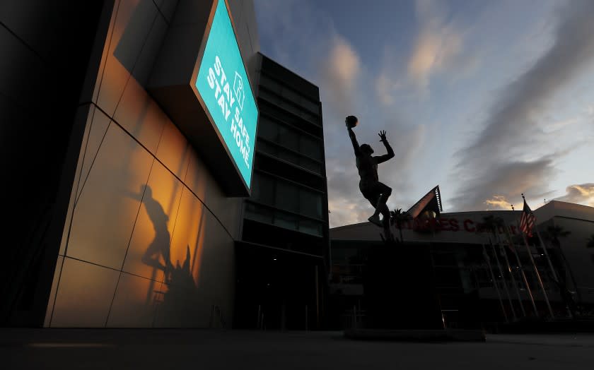 LOS ANGELES, CALIF. - APR. 10, 2020. The shadow of a statue of Magic Johnson, left, and a statue of Kareem Abdul Jabbar putting up a sky hook are frozen in time at Staples Center, where the lights are off and events have been suspended in the wake of the coronavirus pandemic. Wearing face cooverings now is mandatory in the city of L.A. as part of an ongoing effort to curb the spread of coronarivrus. (Luis Sinco/Los Angeles Times)