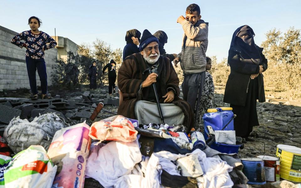 A displaced Palestinian man sits among objects salvaged from his house