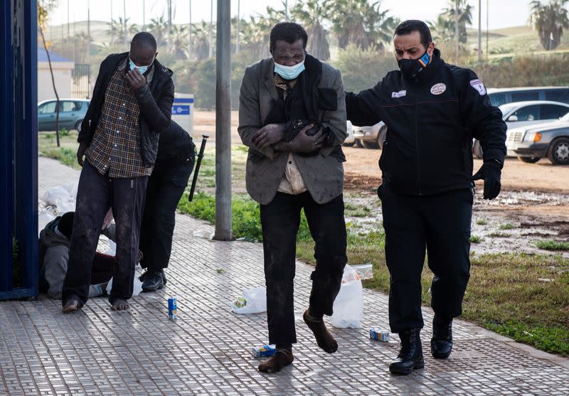 Migrants receive help from security guards as they arrive at the temporary migrants center upon crossing the border fence, in Melilla