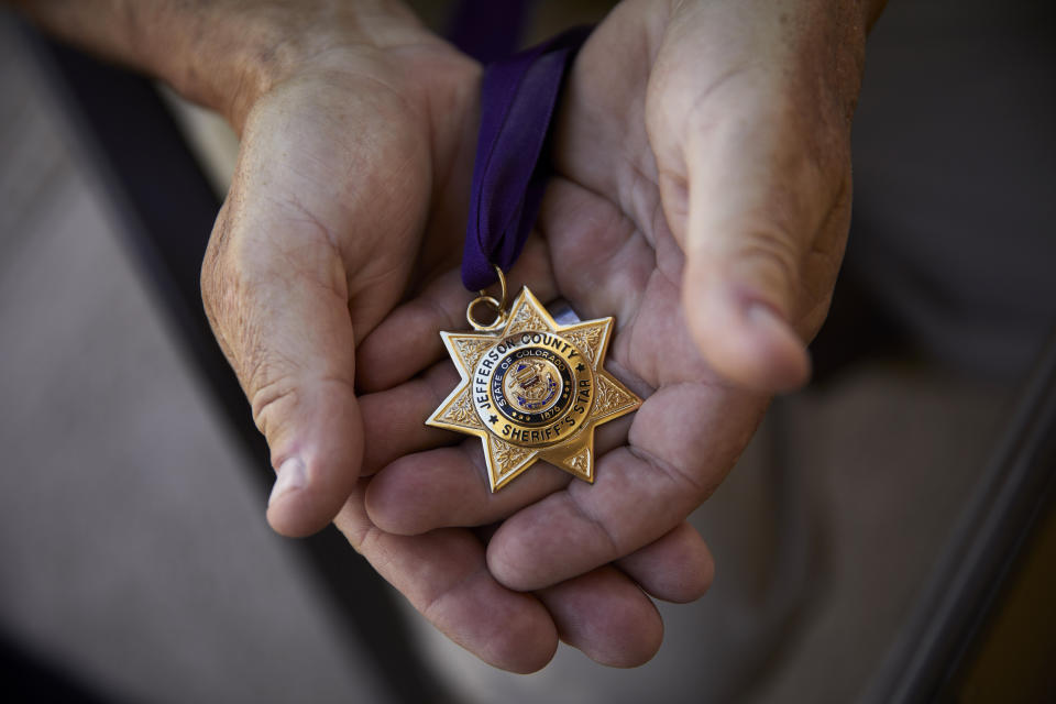 In this April 9, 2019, photo, Grant Whitus holds the Jefferson County Sheriff's Star at his home in Lake Havasu City, Ariz. Whitus received the award for his actions on several incidents while with the Jefferson County Regional SWAT team, including Columbine High School. Whitus' marriage fell apart a year after he led his SWAT team into Columbine High School's library, where he was the first to find the dead children's bodies. (AP Photo/John Locher)