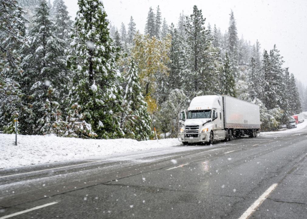 A semi-truck parked on the side of a snowy highway.