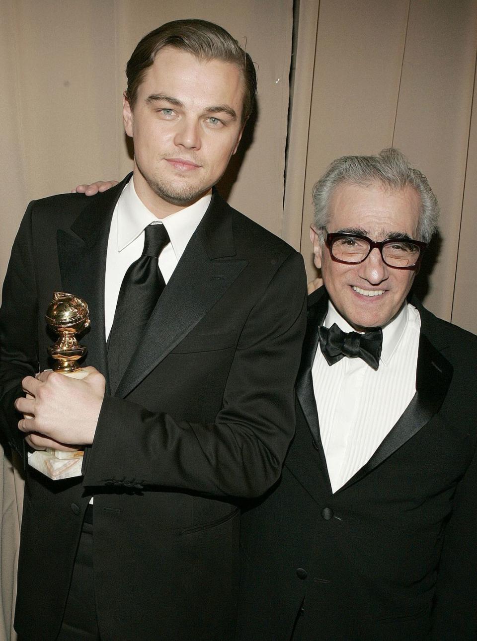 leonardo dicaprio and martin scorsese smile for a photo together while standing, dicaprio holds a golden globe statuette and scorsese has one arm around dicaprios shoulders, both men wear black suits and ties with white collared shirts