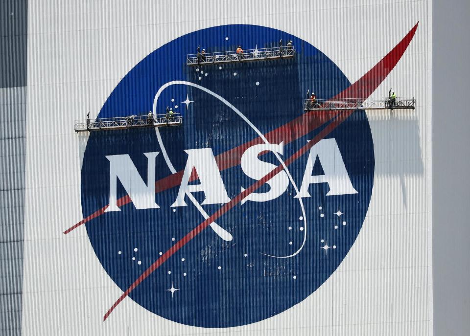 Workers freshen up the paint on the NASA logo on the Vehicle Assembly Building before the arrival of NASA astronauts Bob Behnken and Doug Hurley at the Kennedy Space Center on May 20, 2020 in Cape Canaveral, Florida: Joe Raedle/Getty Images