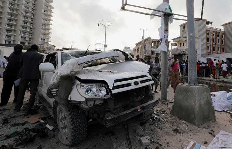 Civilians are seen near the wreckage of a car destroyed at the scene of a militant attack at the Elite Hotel in Lido beach, in Mogadishu