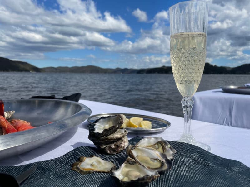 Fresh Sydney rock oysters lie next to a glass of champagne on a table during a tour of an oyster farm. Oyster farmer Sheridan Beaumont offers an oyster lunch in the water with her Sydney Oyster Farm Tour. Michelle Ostwald/dpa