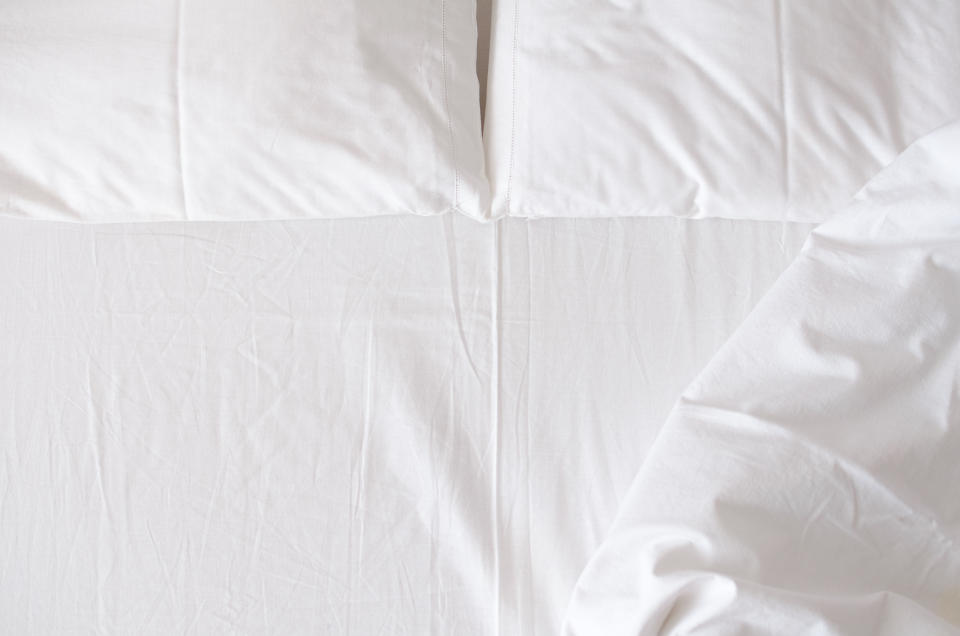 A neatly made bed with white sheets and pillows, with part of the blanket slightly folded over on the right side