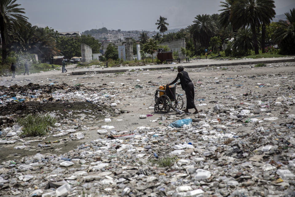 A woman pushes a wheelchair, carrying her empty water containers, through an empty street littered with trash near the judiciary and legislative buildings, in Port-au-Prince, Haiti, Tuesday, Sept. 22, 2021. Most of the population of Port-au-Prince has no access to basic public services, no drinking water, electricity or garbage collection. (AP Photo/Rodrigo Abd)