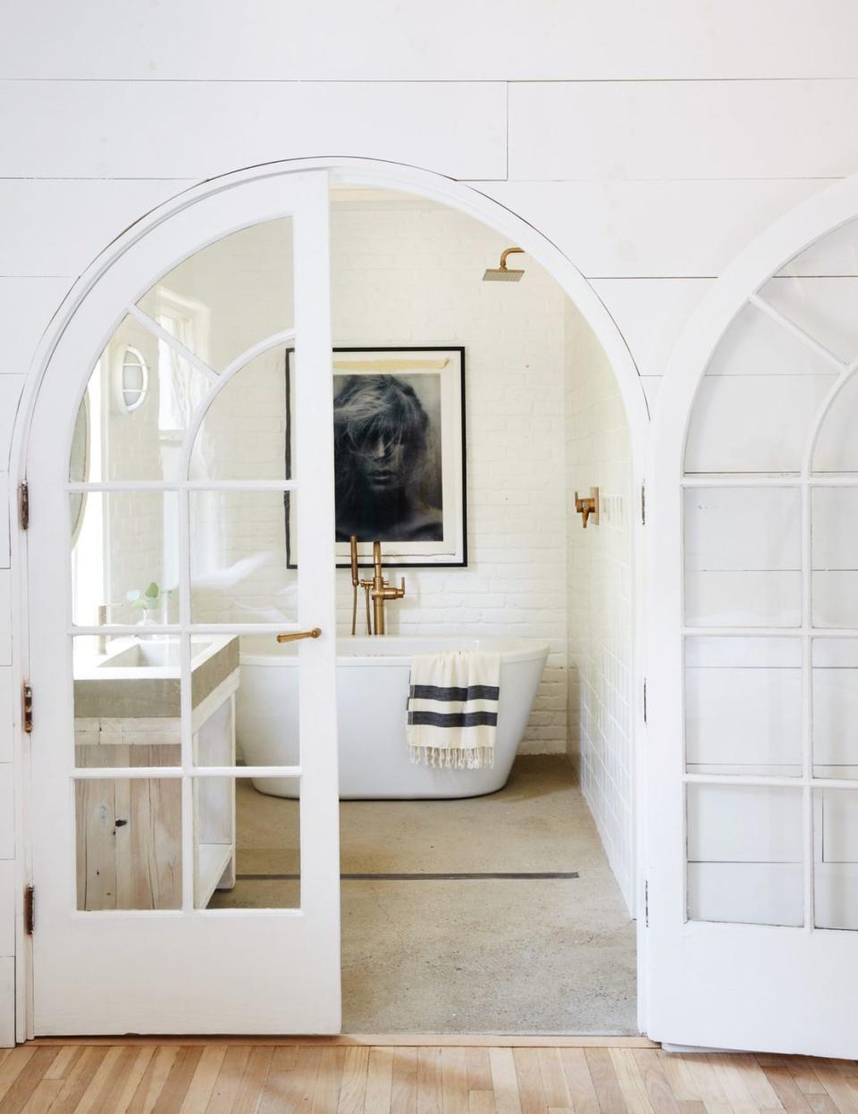 <p>For a romantic, open atmosphere, consider installing glass doors. These white French doors in this main bathroom designed by Leanne Ford draw our eye straight to that dreamy bathtub (the moody artwork above it helps, too). And the concrete floors add an edgy touch. </p>