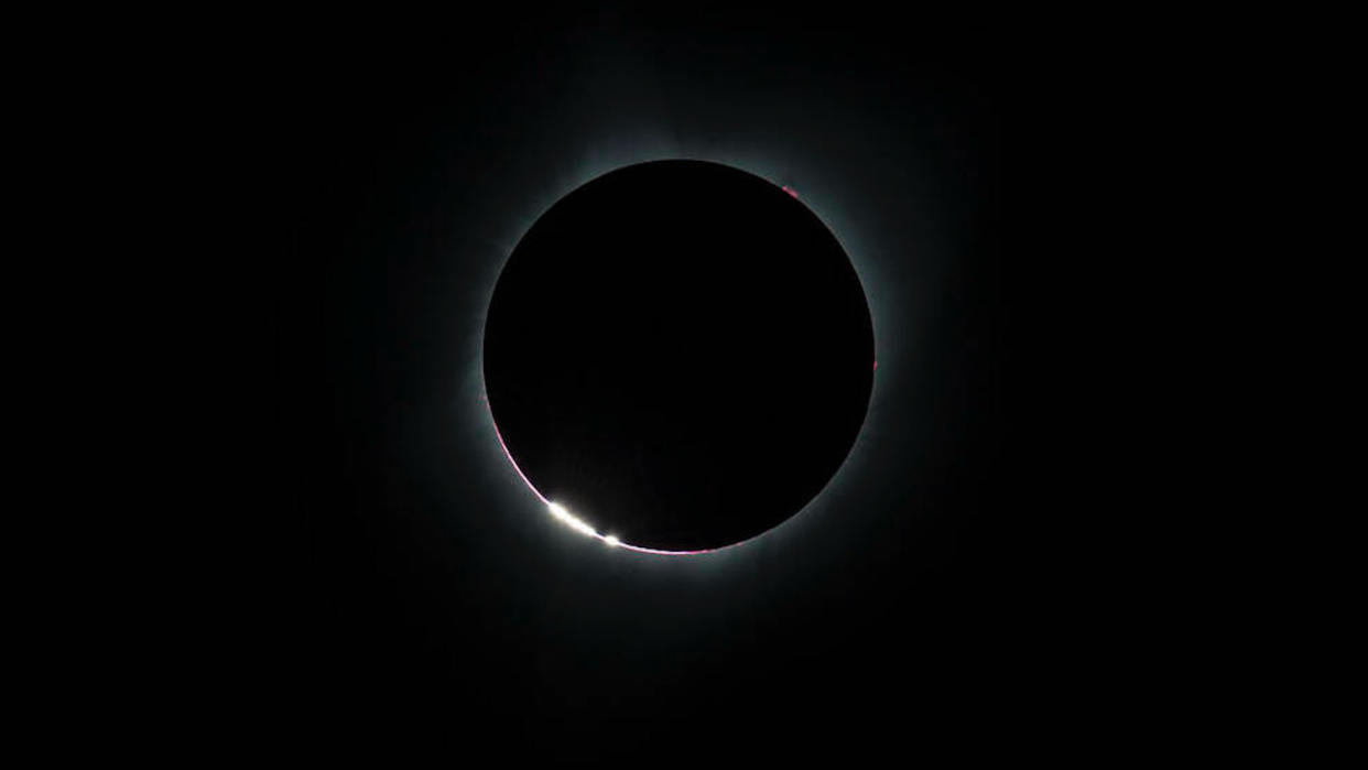  Photo of a total solar eclipse, showing the sun's disk totally blocked out except for a thin whitish-yellow ring. 