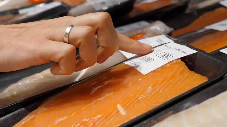 Finger pointing at a label on a package of raw salmon