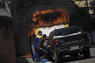 Men move a car away from a burning bus that was set on fire near the area recently occupied by squatters in Rio de Janeiro, Brazil, Friday, April 11, 2014. Squatters in Rio de Janeiro are clashing with police after a Brazilian court ordered that 5,000 people be evicted from abandoned buildings of a telecommunications company. Officers have used tear gas and stun grenades to try to disperse the families. (AP Photo/Felipe Dana)