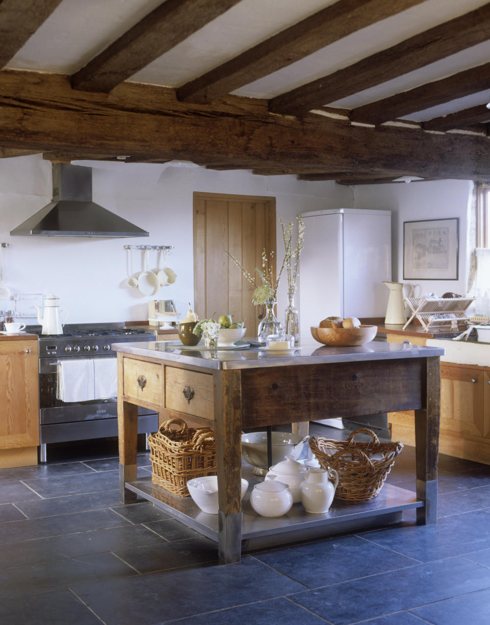 A rustic wooden portable kitchen island in a farmhouse kitchen with dark gray slate flooring.