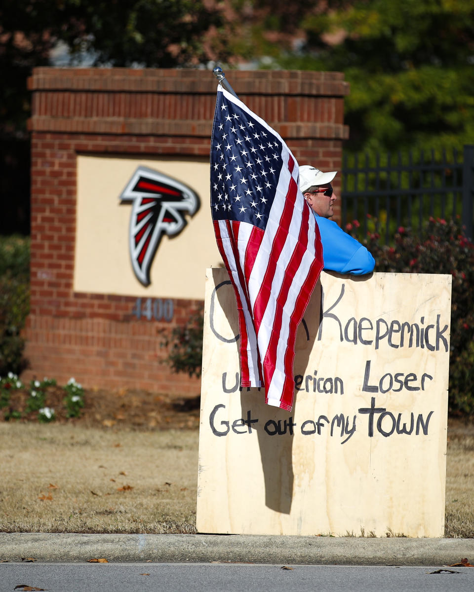 A protester holds an American flag and a sign outside of the Atlanta Falcons' training facility where free agent quarterback Colin Kaepernick was set to workout for NFL football scouts, Saturday, Nov. 16, 2019, in Flowery Branch, Ga. The workout was moved to a high school in Riverdale, Ga. (AP Photo/Todd Kirkland)