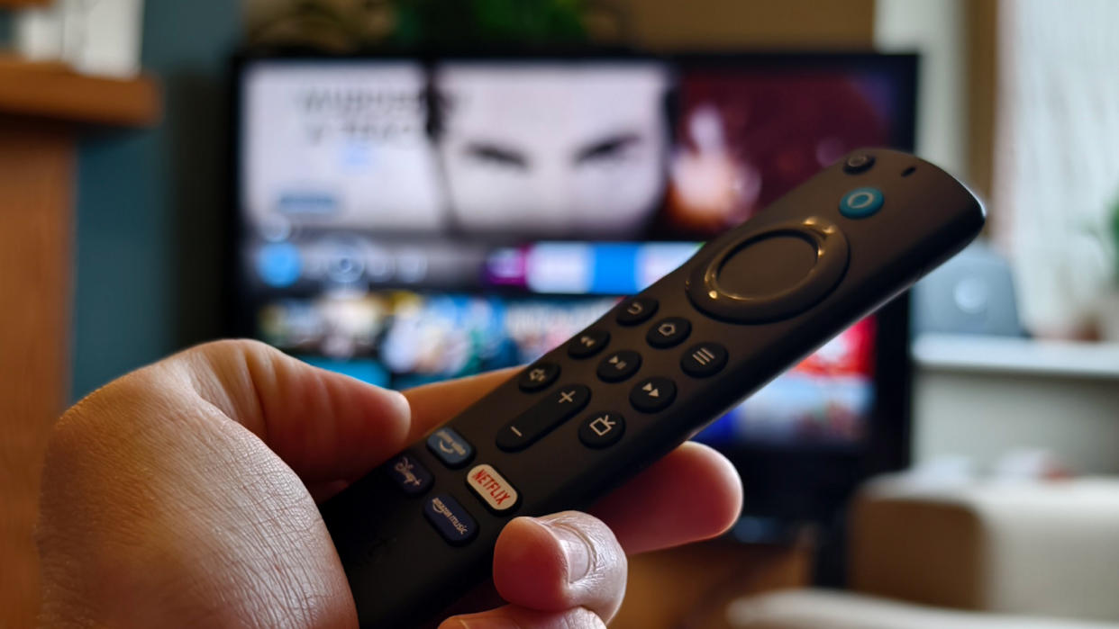  The Amazon Fire TV Stick being held in front of a TV displaying Fire OS. 
