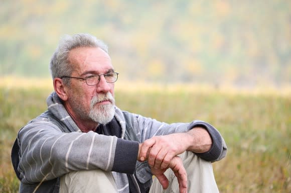 Older man with concerned expression sitting in an outdoor field.